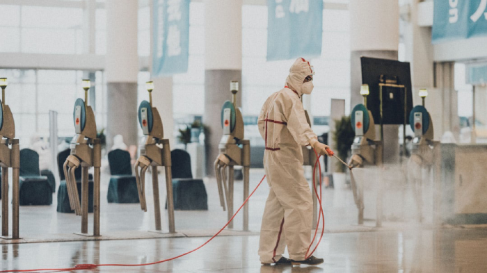 Unidentifiable person in white overalls disinfects a public space