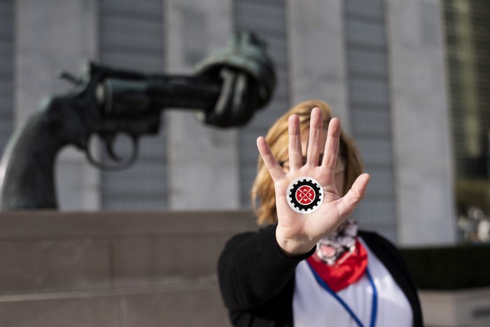 Un activista lleva la mano a la cámara con el logotipo de Stop Killer Robot en la mano frente a la escultura de la pistola anudada.