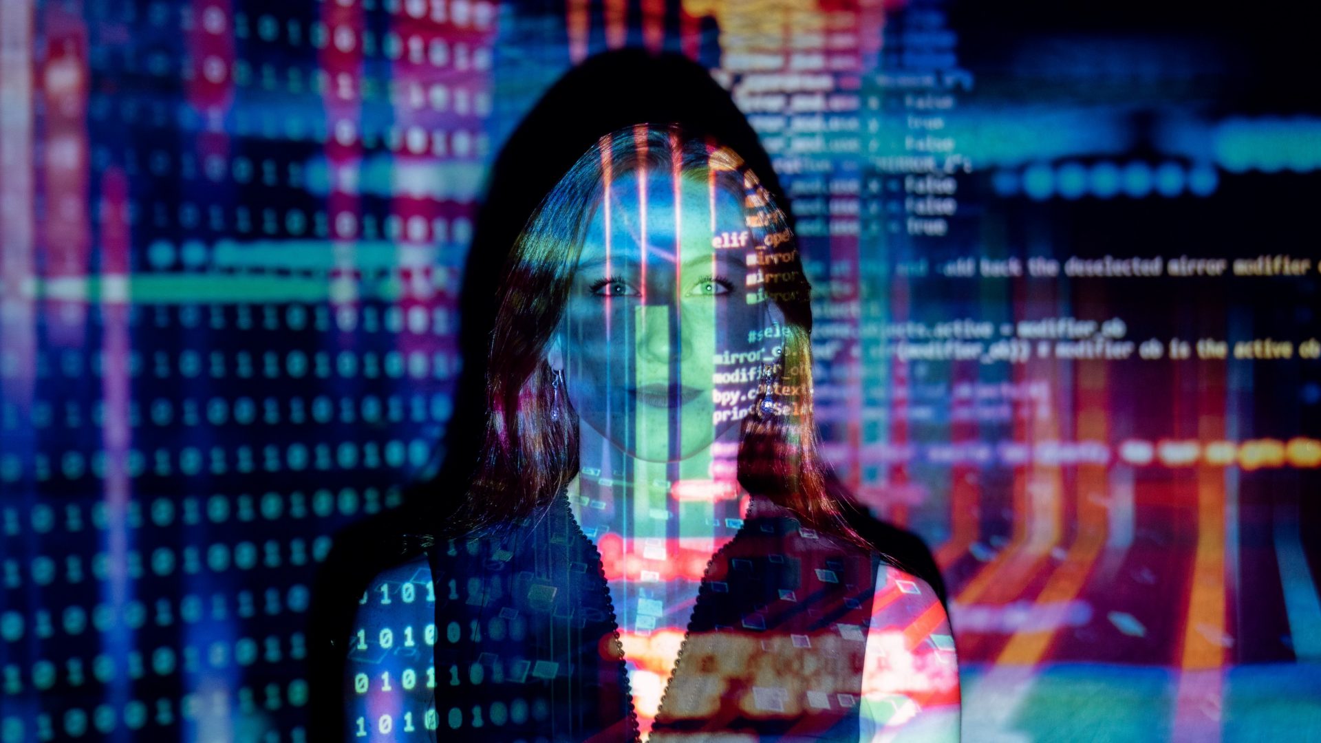 A female software engineer looks directly at the camera with colourful code projected on her.