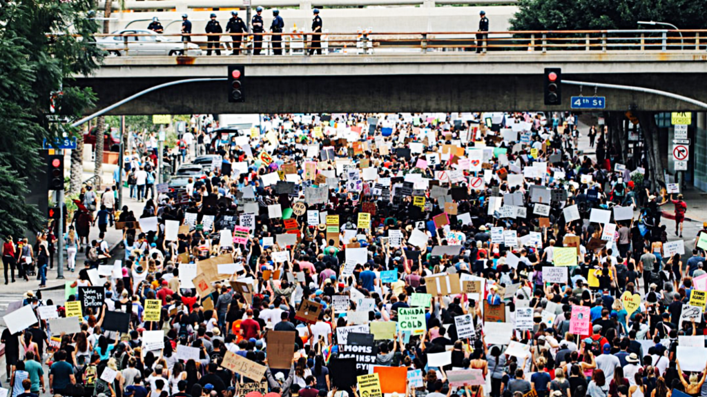 Colourful peaceful protest march walking under a bridge as police officers on the bridge look down