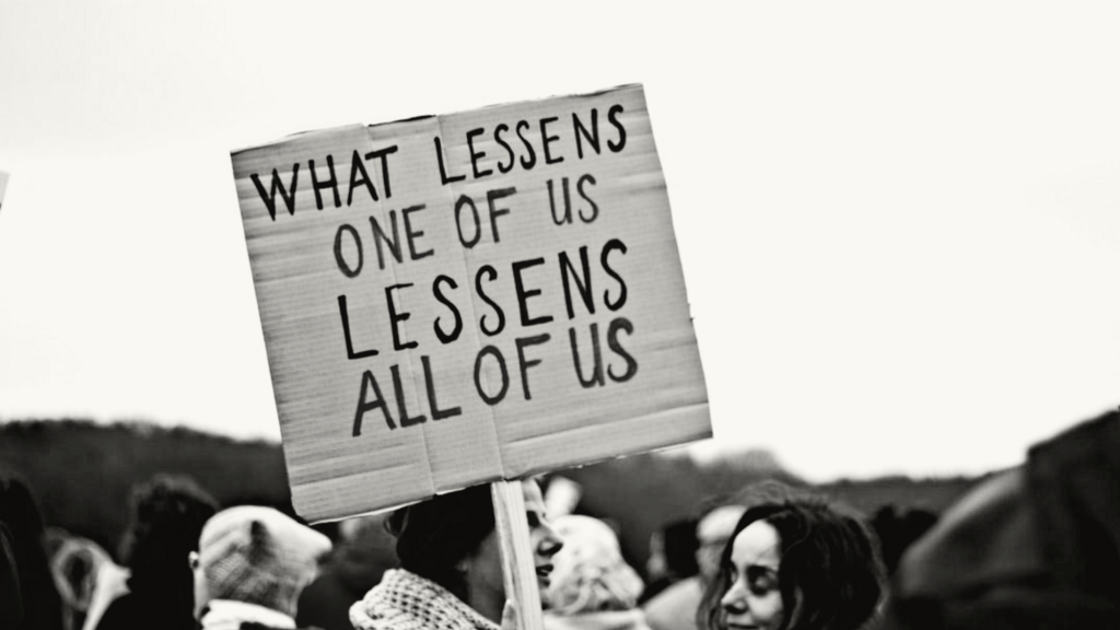 Protest sign reads ‘What lessens one of us lessens all of us’.