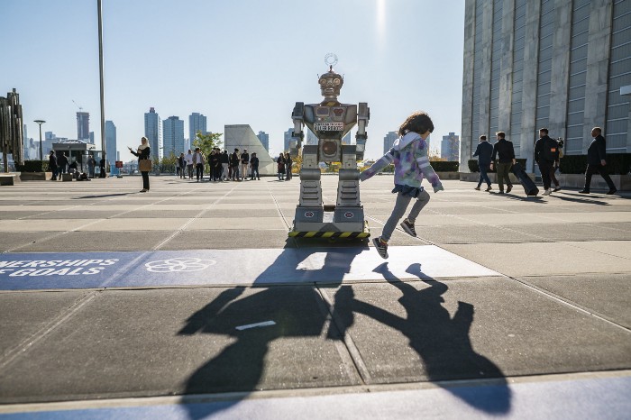 A child skips past the Campaign to Stop Killer Robots robot in front of the UN in New York, they both cast long shadows